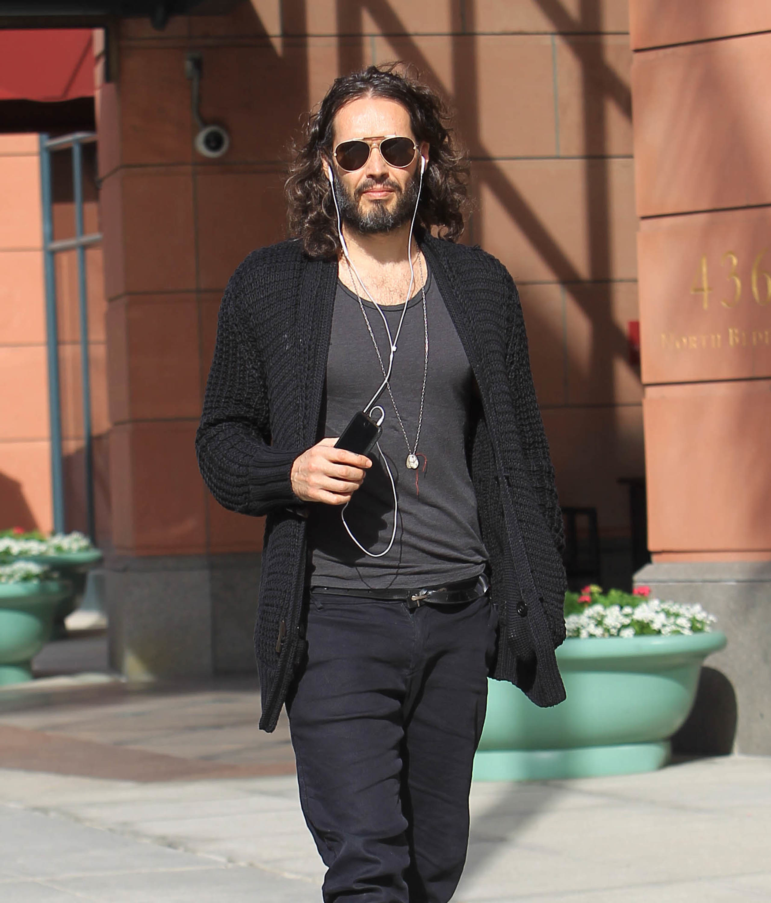 Russell Brand walking down the street while listening to music