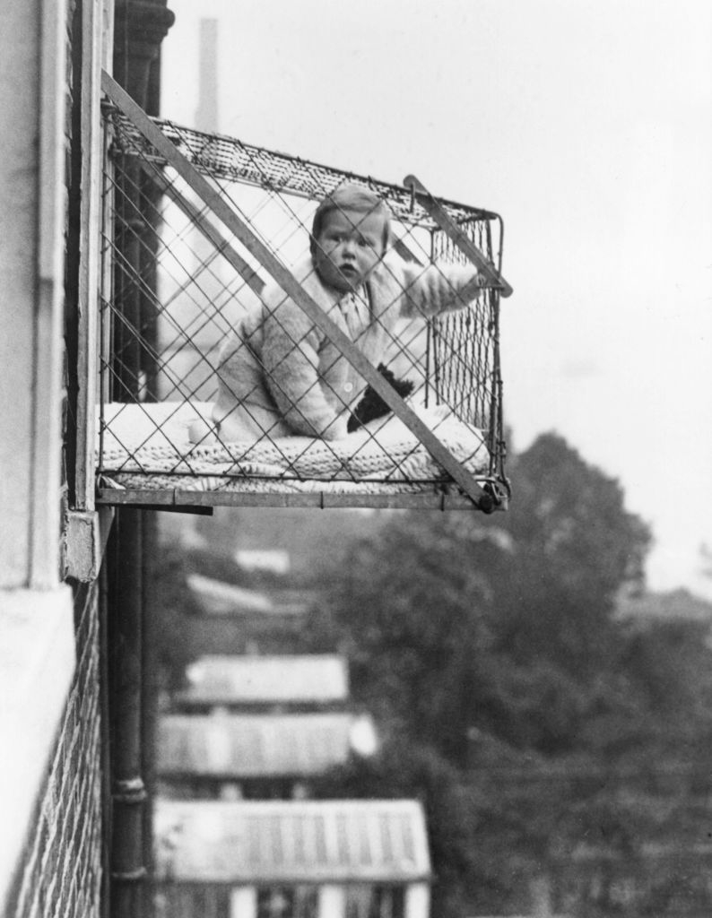 A baby in a cage that looks like an air conditioner chassis outside a window