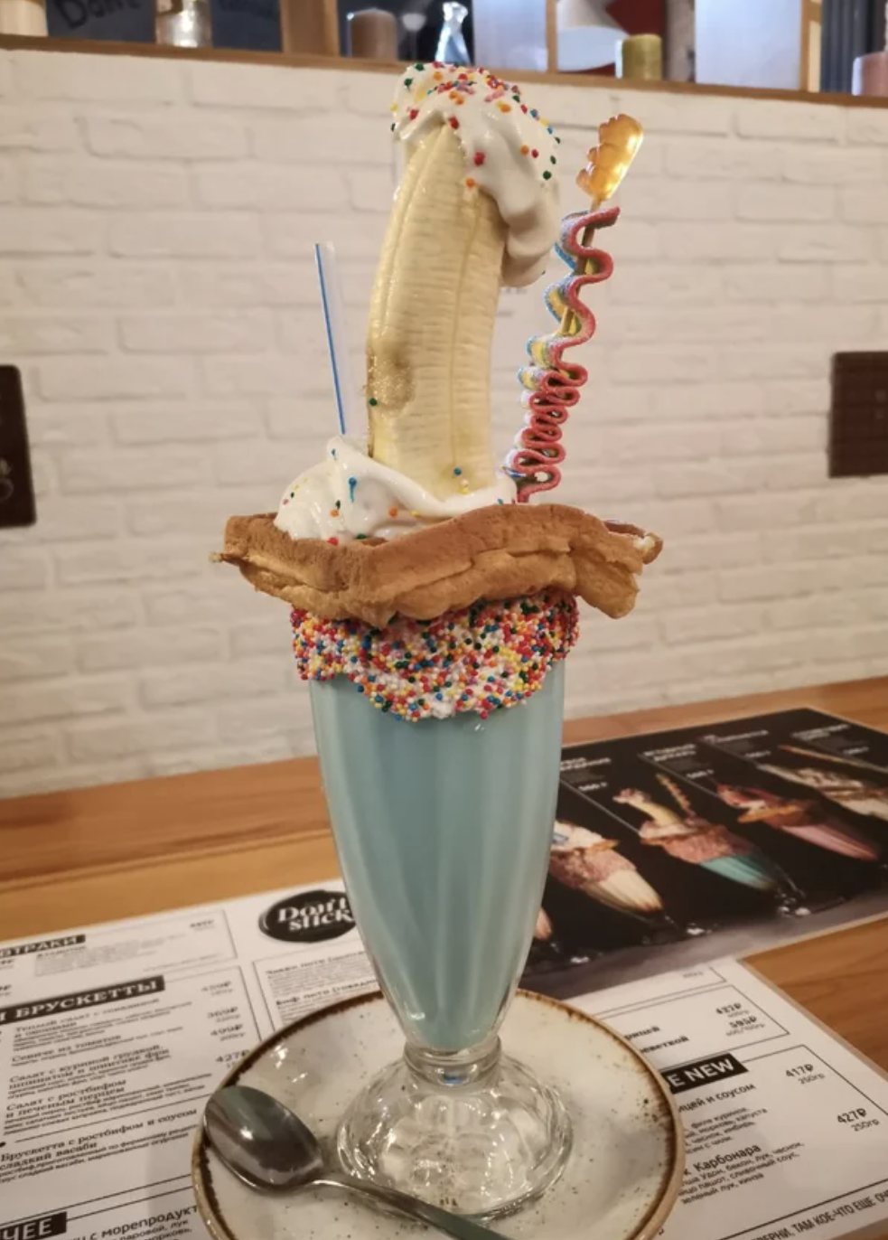 A milkshake is stacked with sprinkles, a waffle, a banana, sour candy, and whipped cream