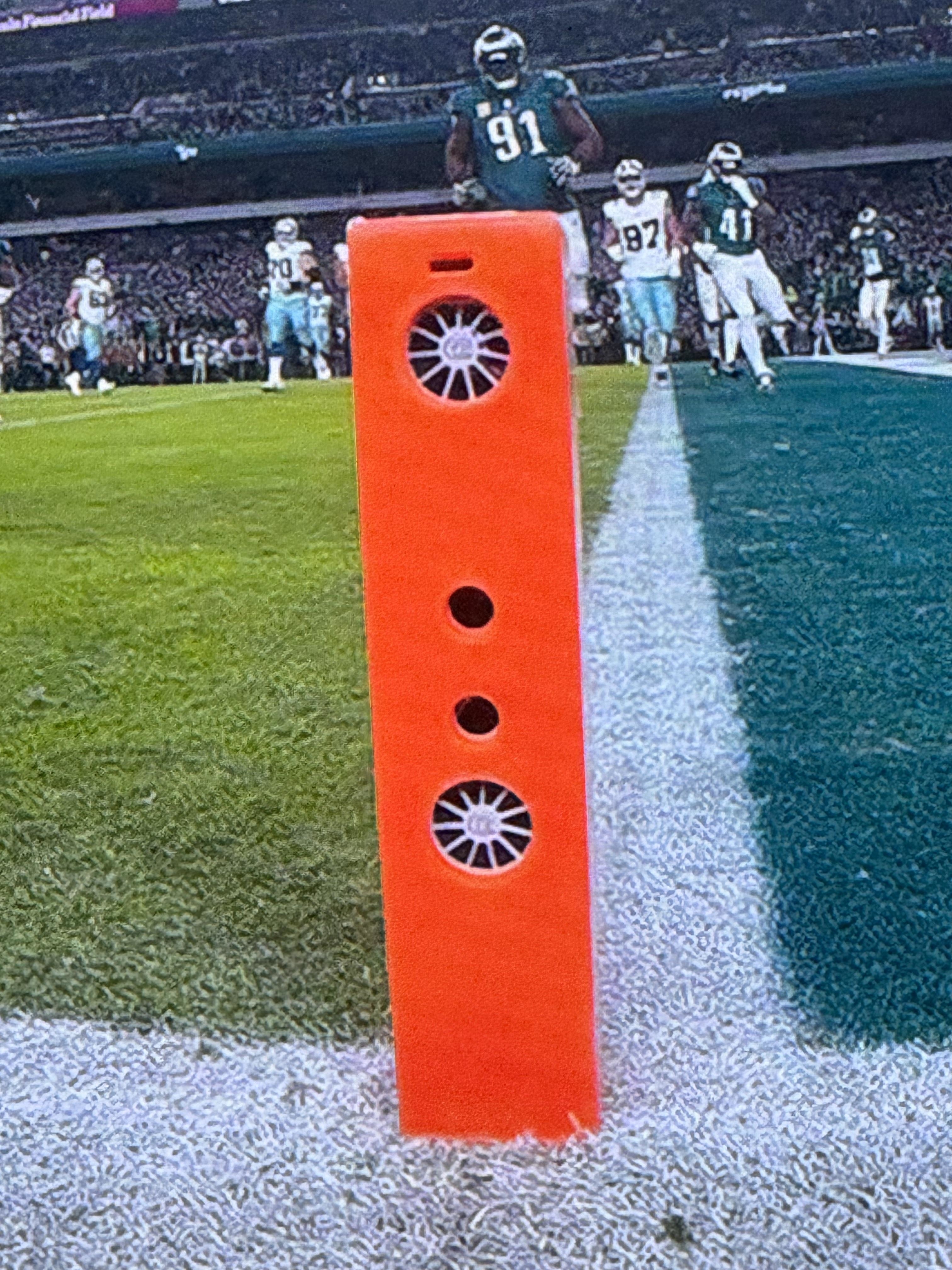 A tall thin, orange post on a football field showing circular openings for fans