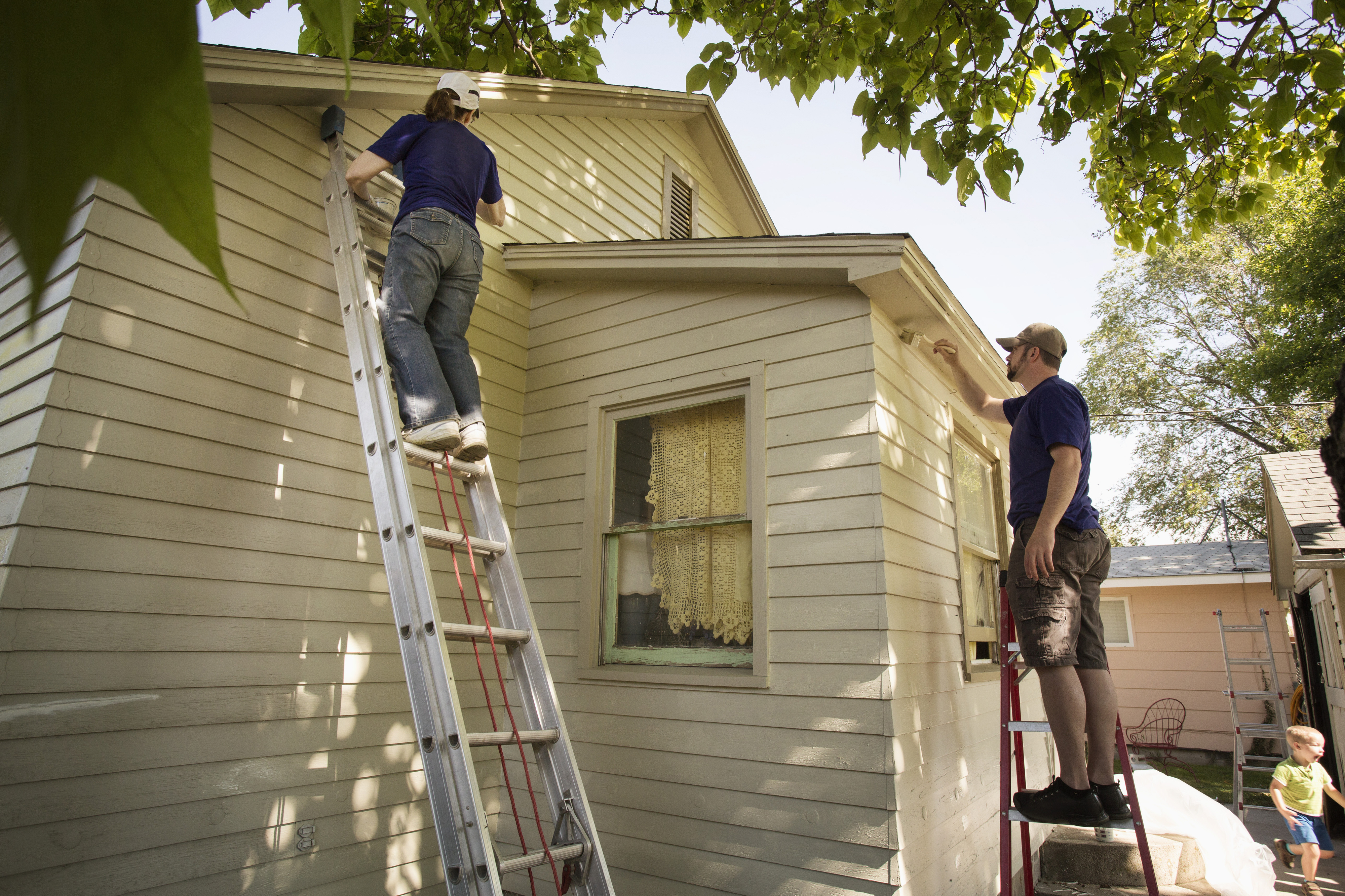 people doing work outside a house on two ladders, looking at the roof