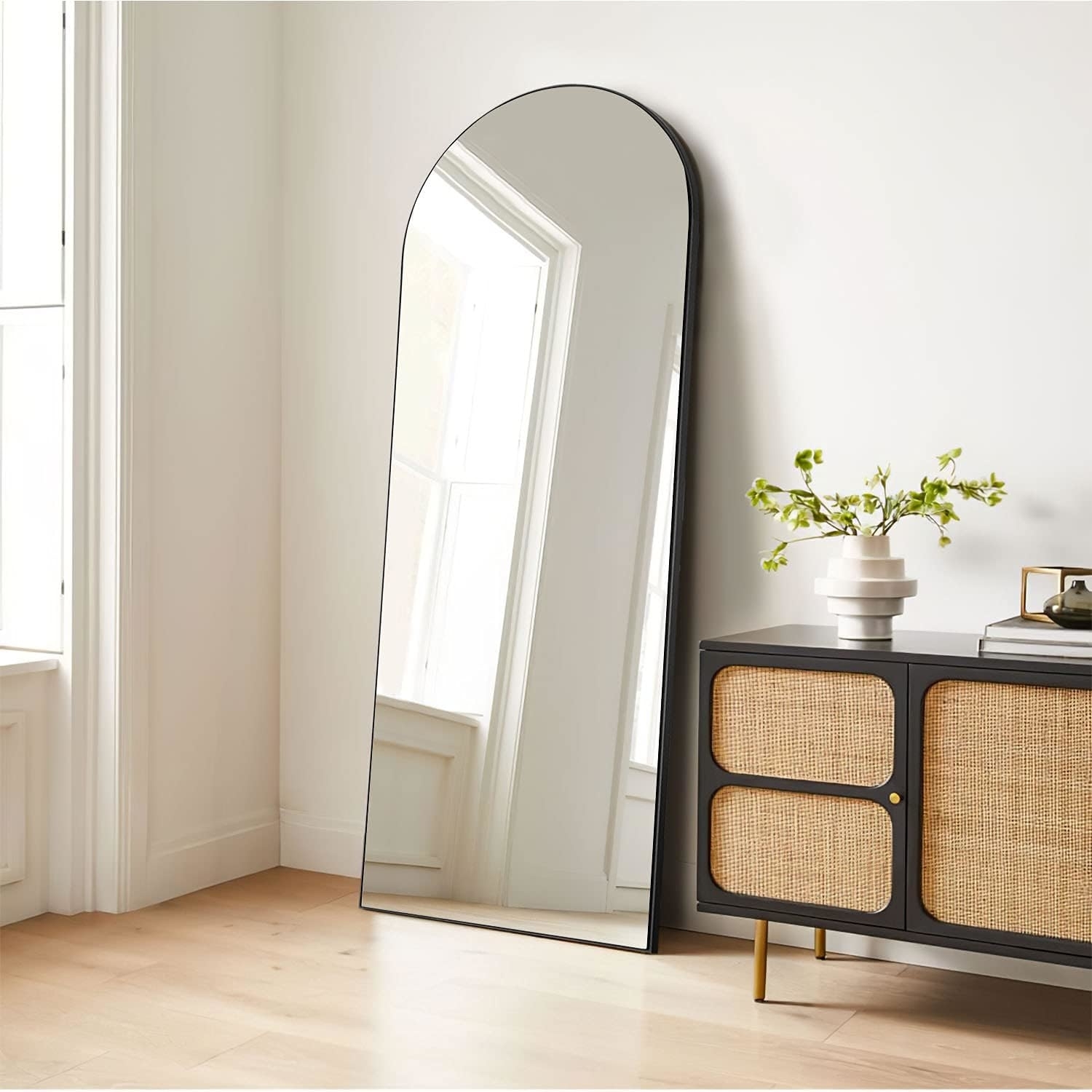 black round arch-top mirror leaned against a wall next to a console table