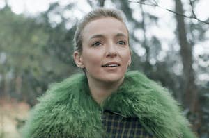 Jodie Comer wears a thick, fluffy jacket while standing in a forest in autumn