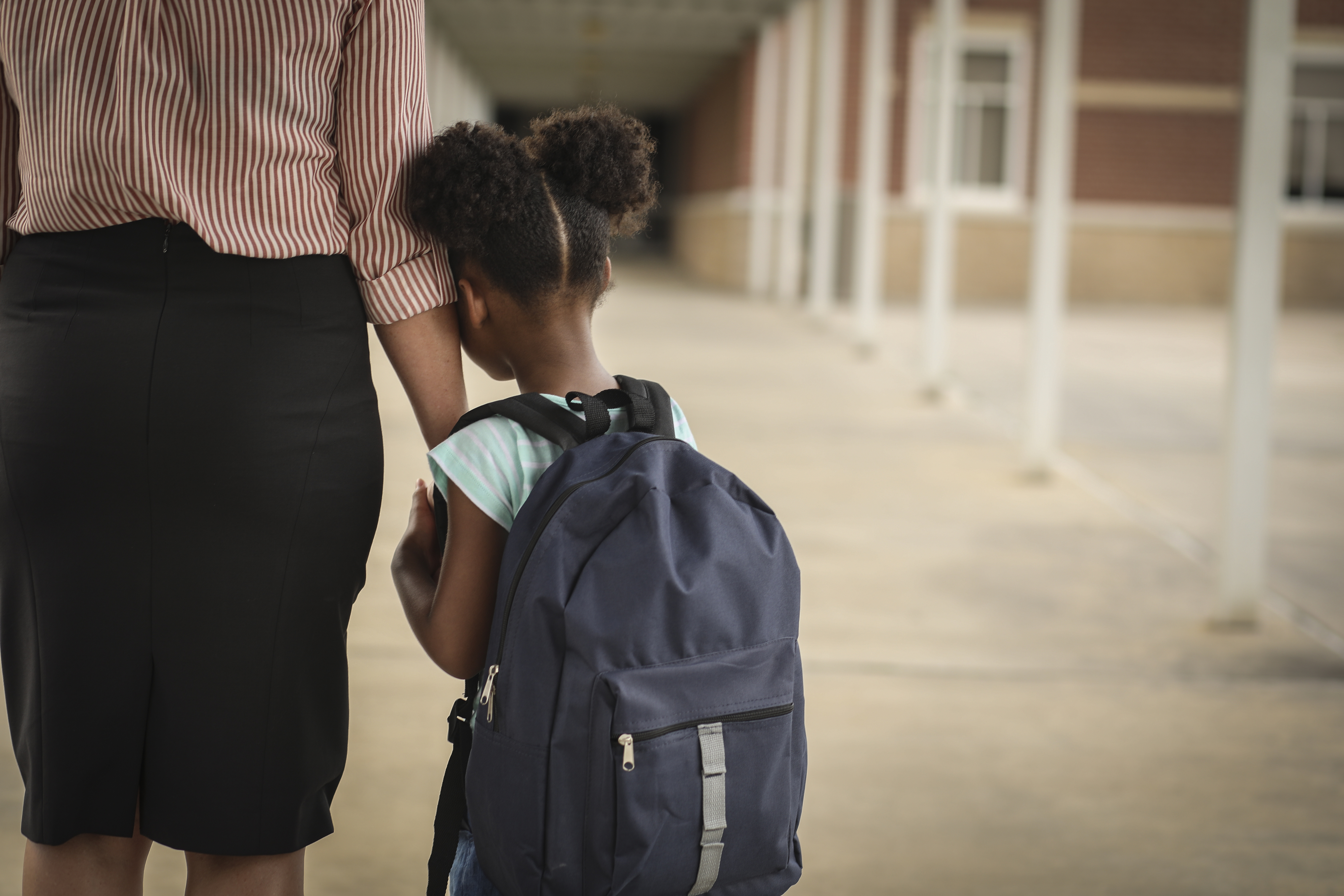 anxious little girl clinging to her mom's hand at school drop off