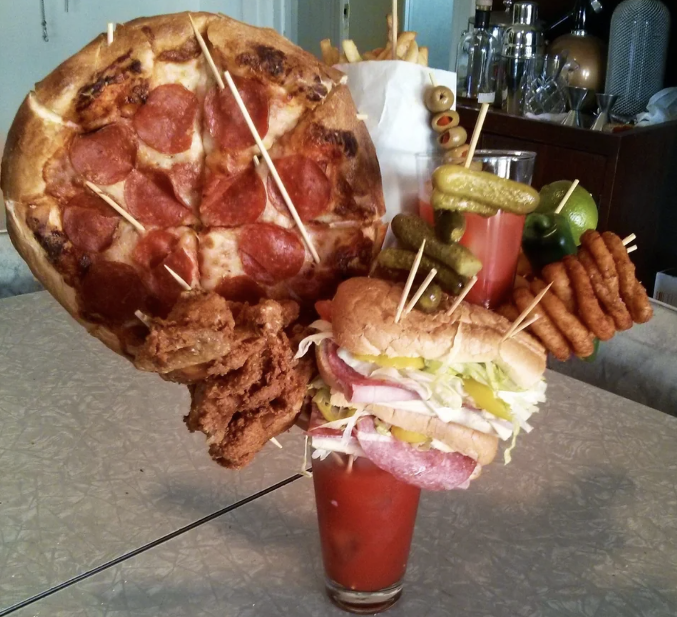 A Bloody Mary is garnished with a pizza, a sandwich, onion rings, chicken wings, pickles, olives, french fries, and a lime