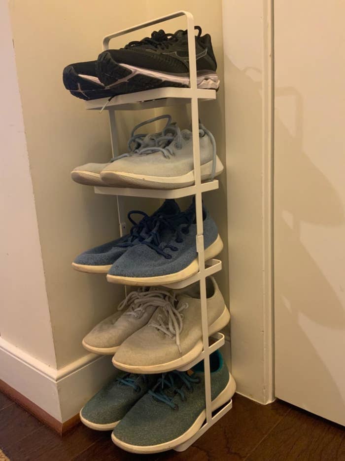 a reviewer photo of the white shoe rack next to a door loaded up with five pairs of sneakers