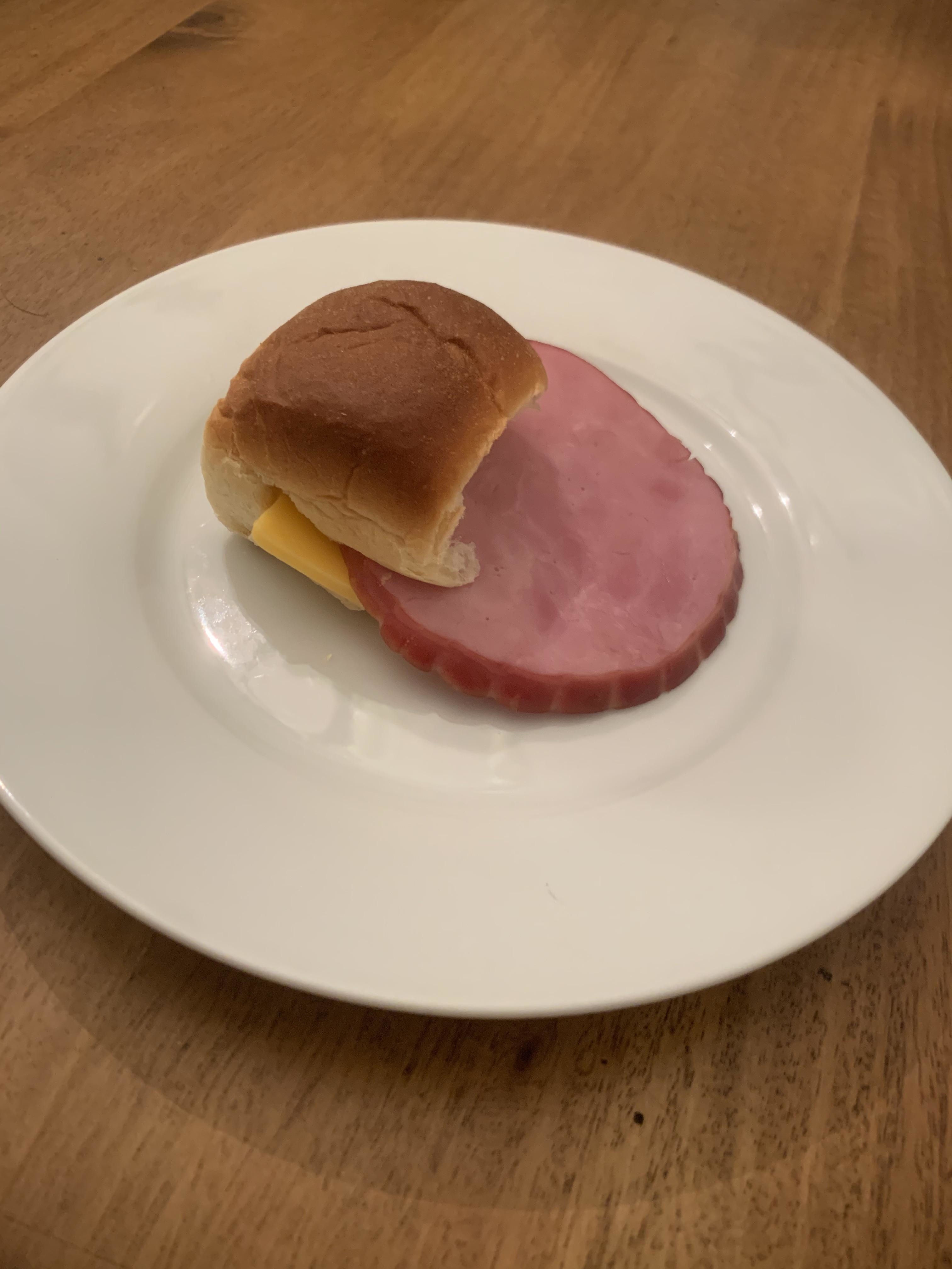 a small hawaiian roll with a large slice of baked ham sticking half out of it