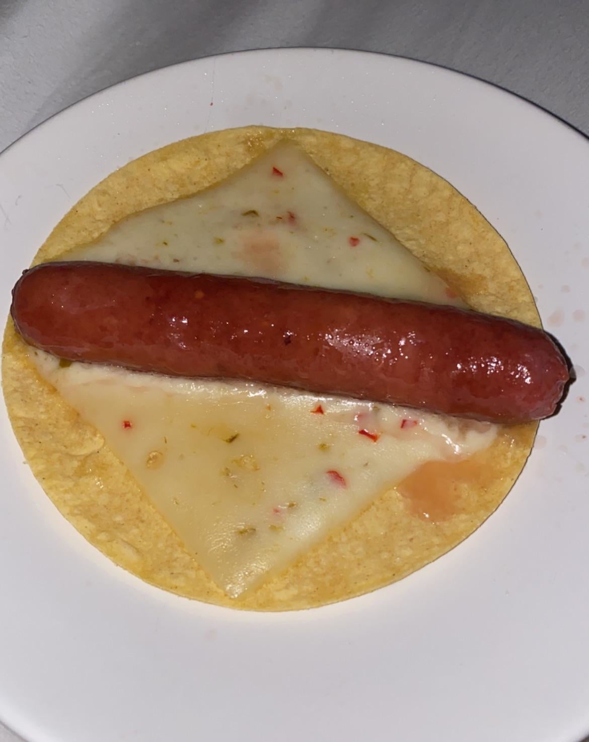 a corn tortilla with a slice of pepper jack and a hot dog on top