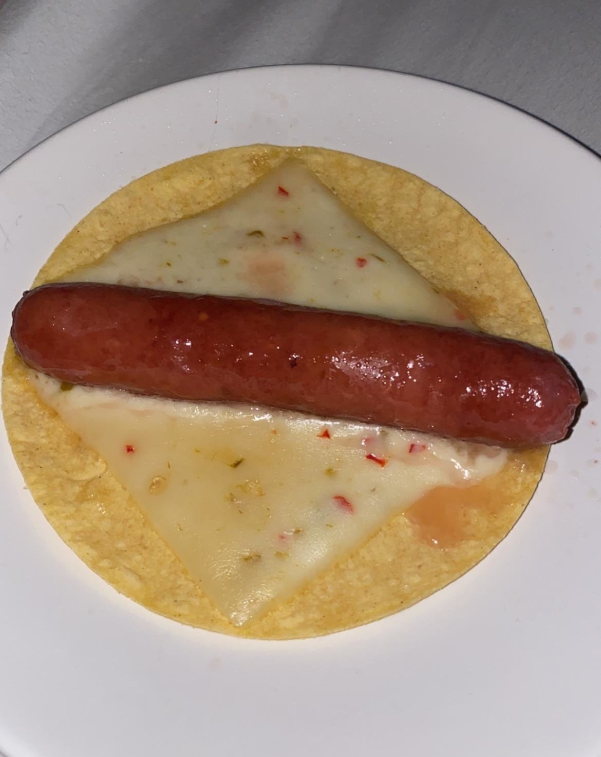 a corn tortilla with a slice of pepper jack and a hot dog on top