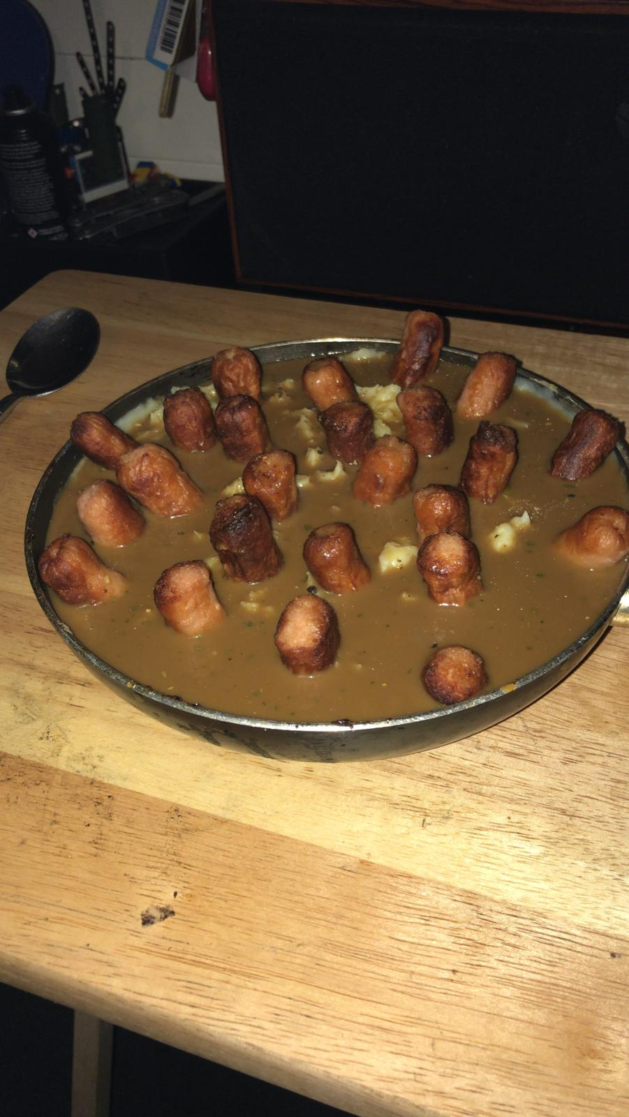 a huge bowl filled to the top with gravy and a bunch of banger sausages sticking out of it