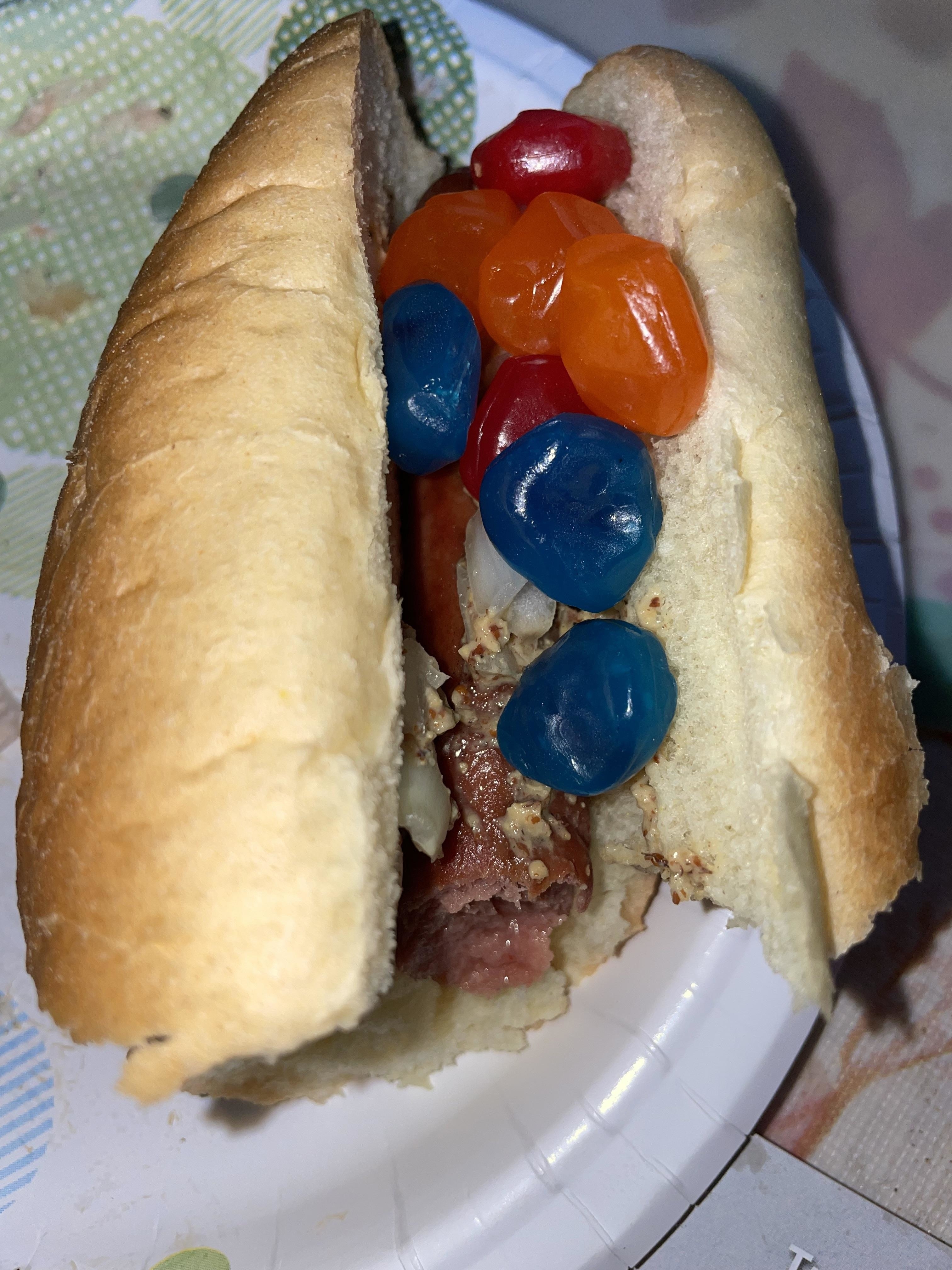 A half eaten hot dog with half a dozen gushers candies on it