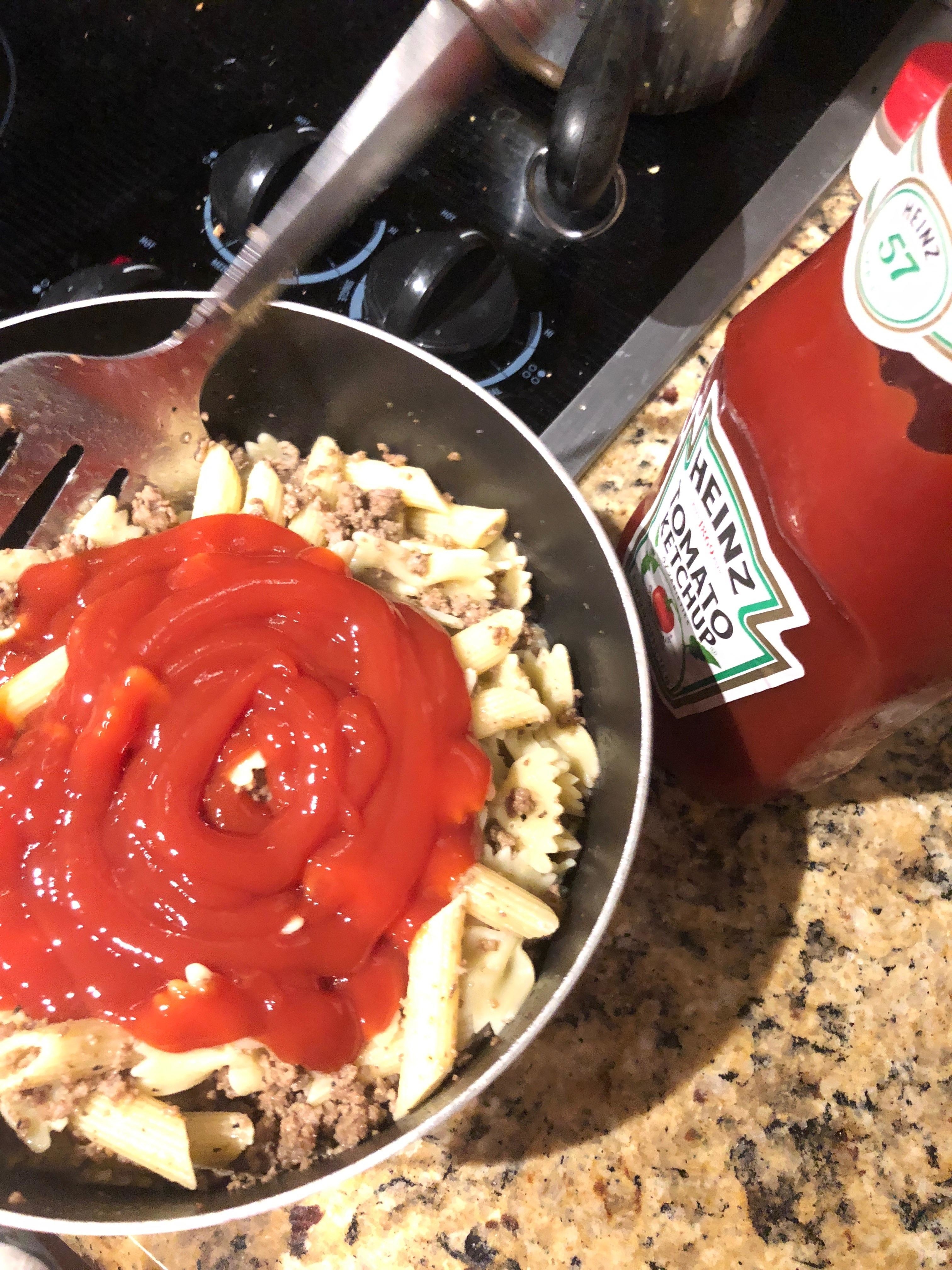 a bowl of penne with some ground beef and a lot of ketchup covering it