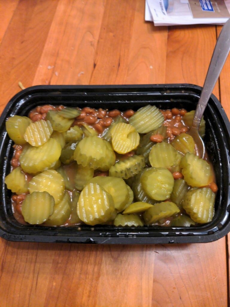 a plastic container with hamburger pickles and beans in a soupy mix