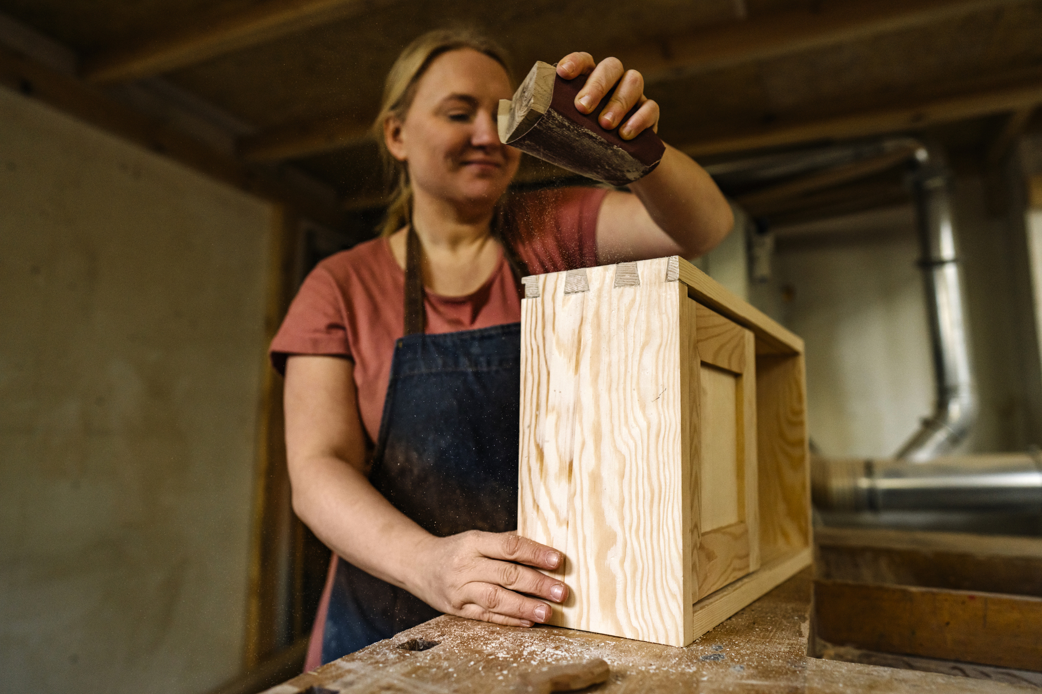 Young entrepreneur sanding hand made wooden drawer in her workshop