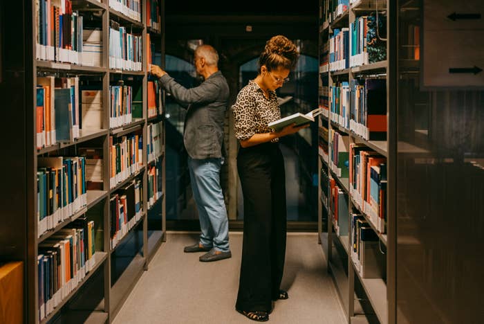 Two people browse books in between two library shelves