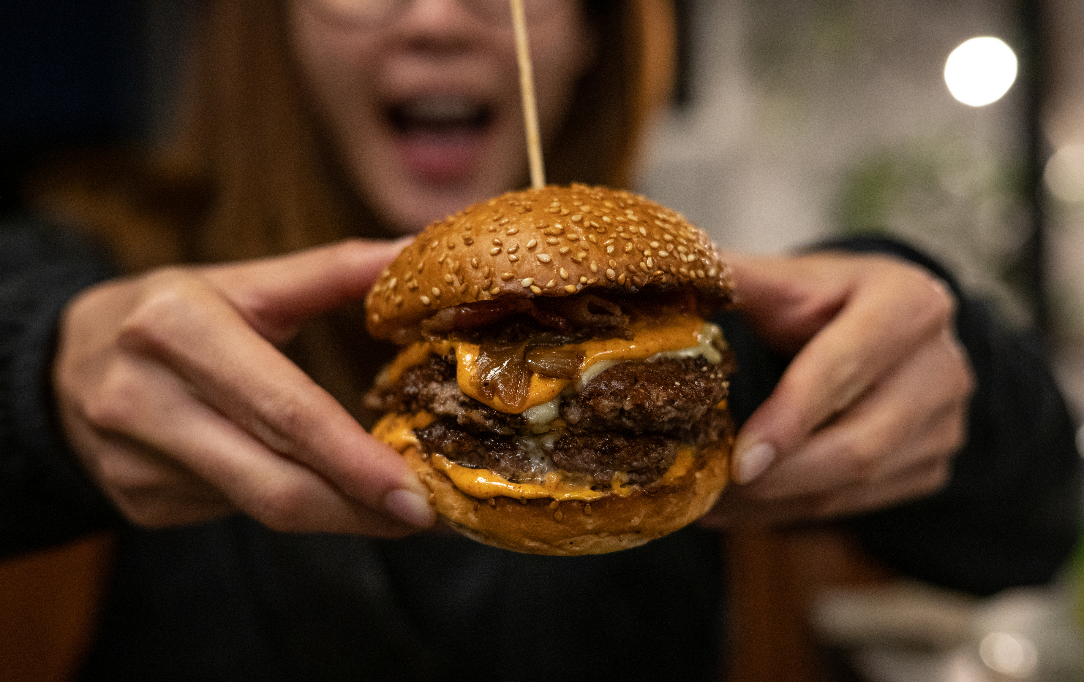 Closeup of a woman&#x27;s hands holding a giant burger with multiple patties