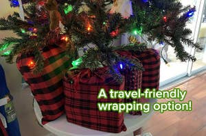 a reviewer photo of gifts inside plaid fabric drawstring bags under a tabletop Christmas tree and text reading "A travel-friendly wrapping option!"