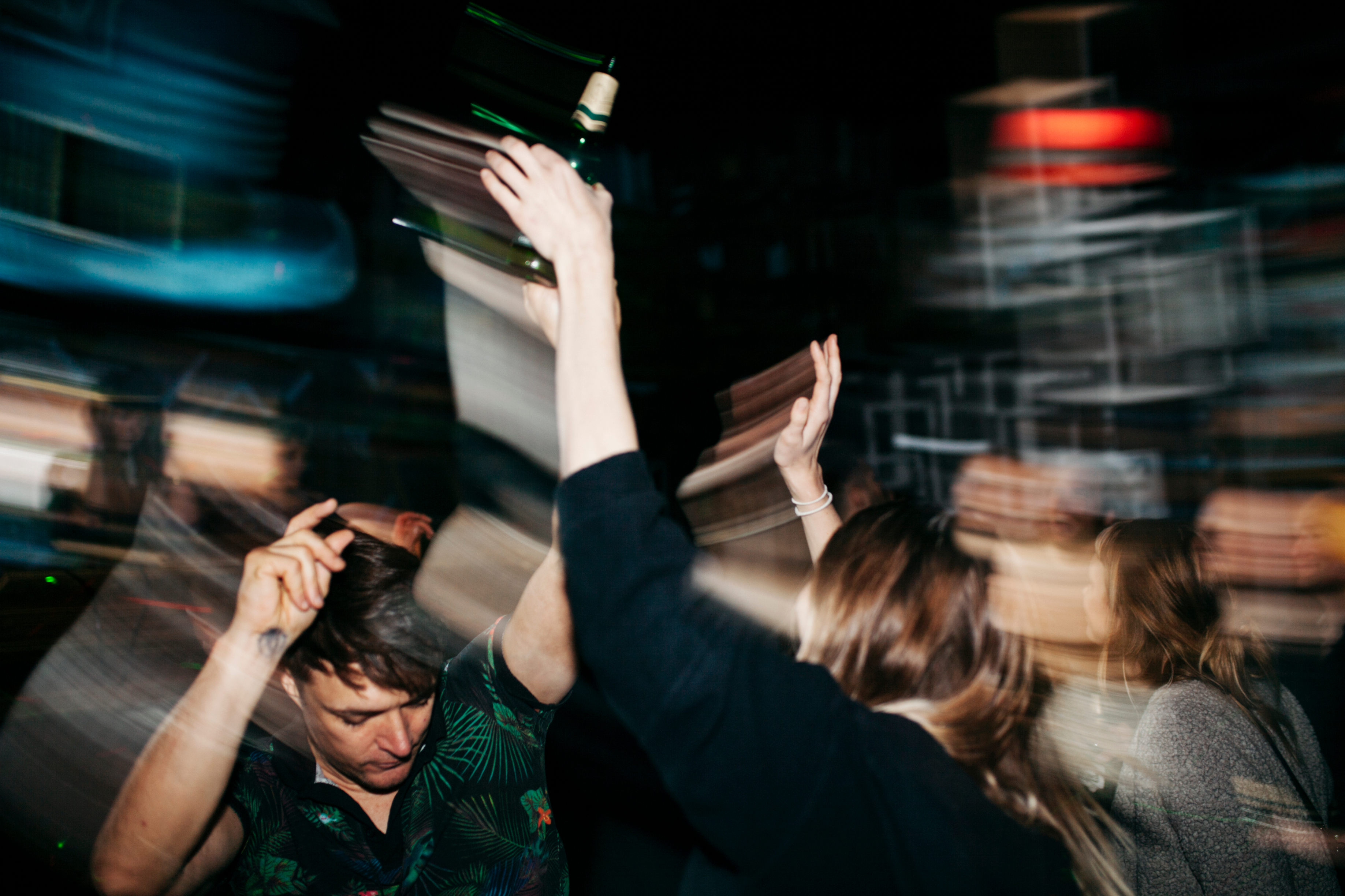 blurry to convey drunkenness; people dance in a crowded nightclub; one person has a bottle in their hands
