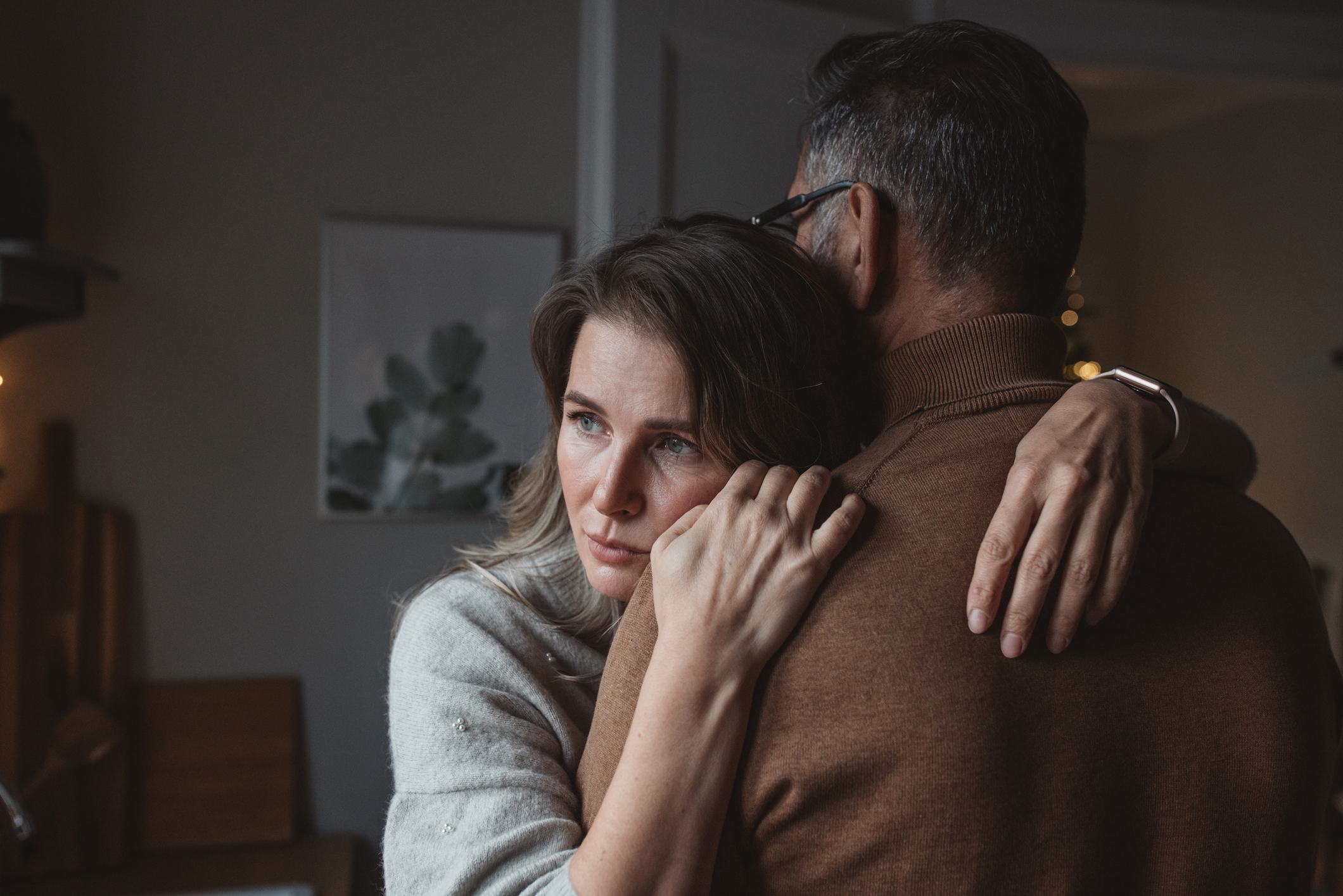 A woman is looking pensive while hugging her husband