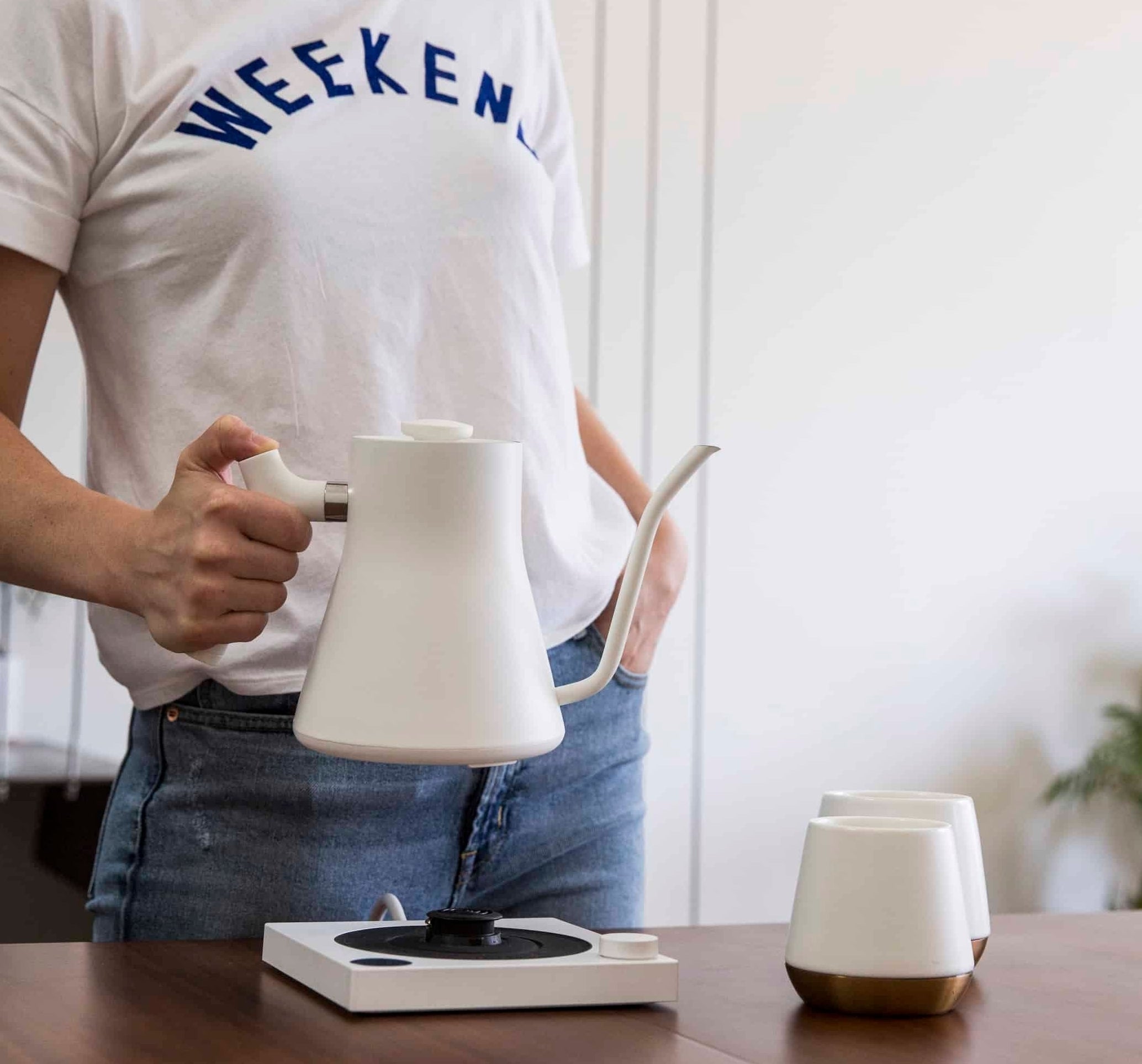 model holding a white gooseneck kettle above its stand