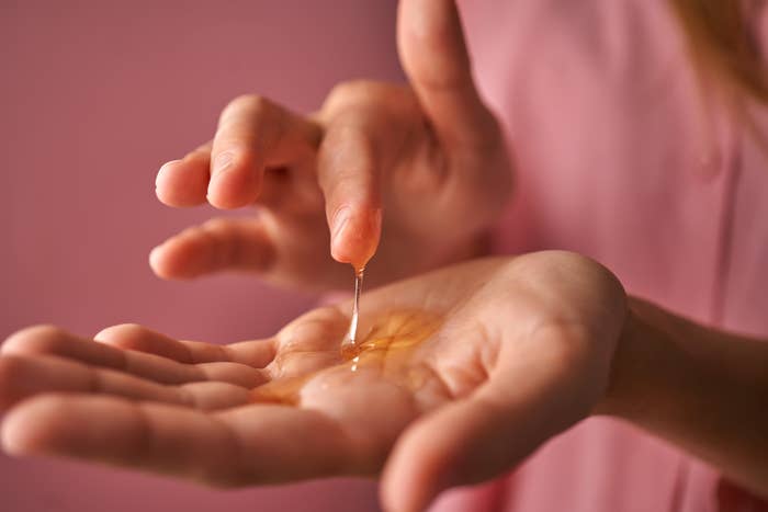 A girl in pink touches a gel cosmetic in her palm with her finger.