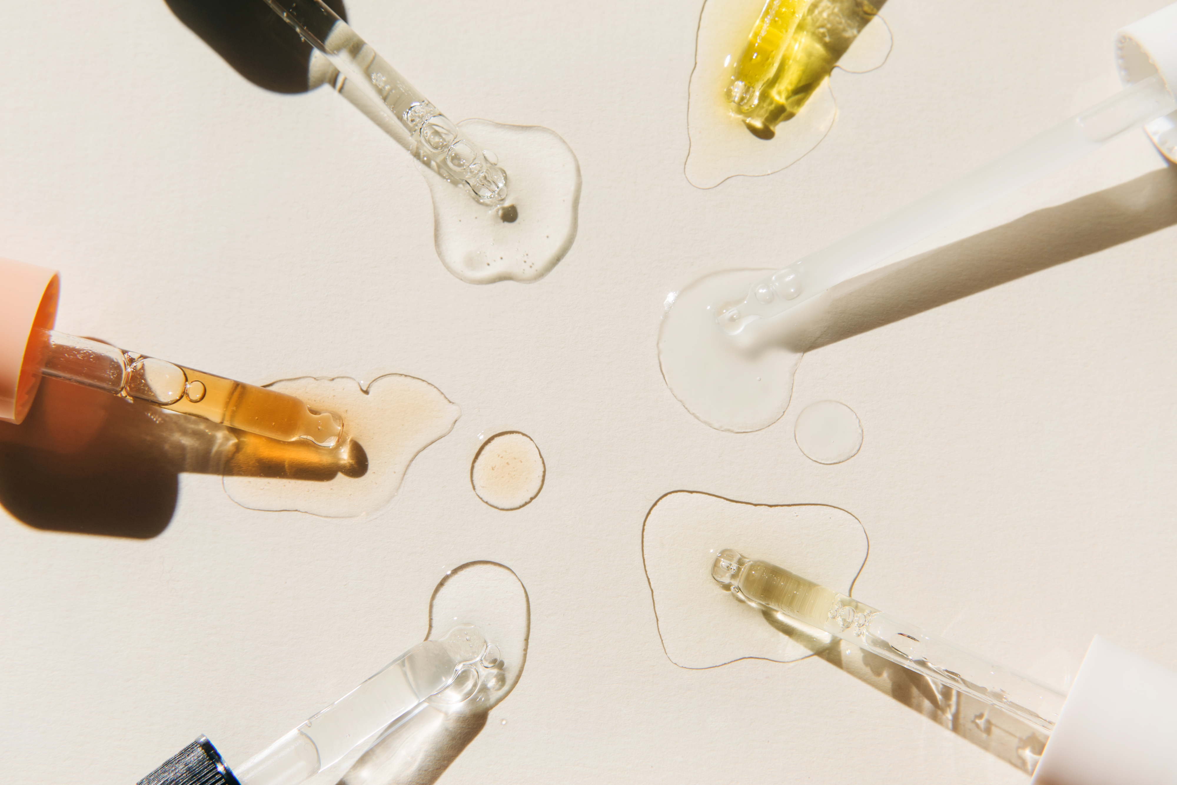 Pipettes with drops of cosmetic liquid on beige background. Beauty product with peptides, ceramides, hyaluronic gel, polyglutamic acid, essential oil, CBD, retinol, collagen. Multitasking beauty. Flat lay, top view.