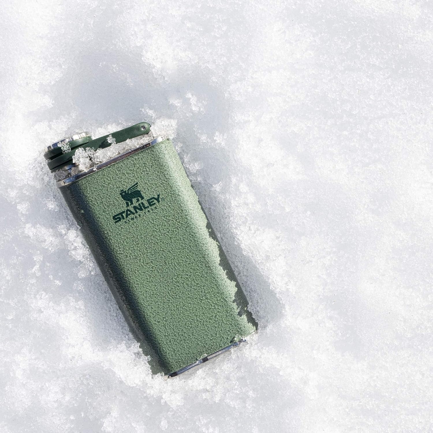 green Stanley flask in pile of snow