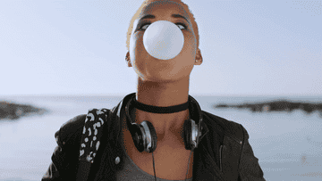A person wearing headphones around their neck and blowing bubbles with bubble gum