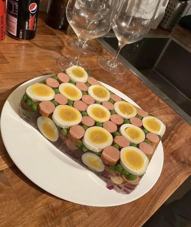 an aspic with hotdogs, sliced boiled eggs, and peas arranged in a mosaic pattern