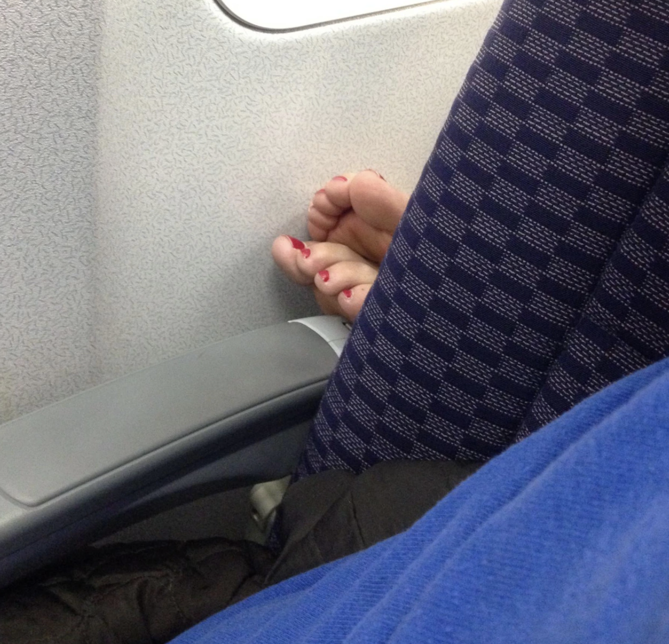 A woman&#x27;s feet is perched on a stranger&#x27;s armrest