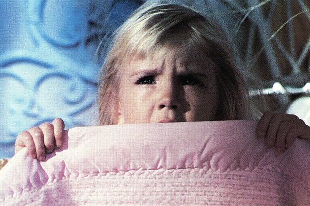 A little girl hiding behind a blanket.