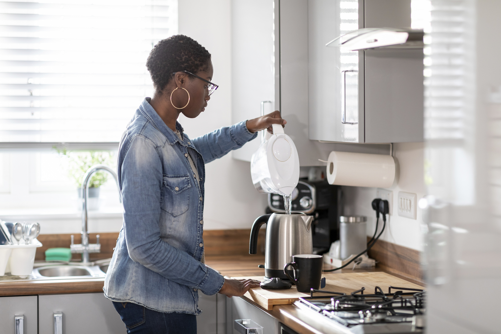 A woman pouring water into her coffee maker in her kitchen