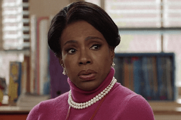 Woman with short hair and pearls and a turtleneck raises her brow as if confused.