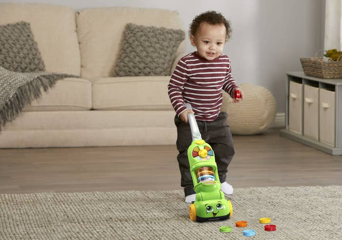 boy pushing mostly green vaccum that sucks up toy pieces