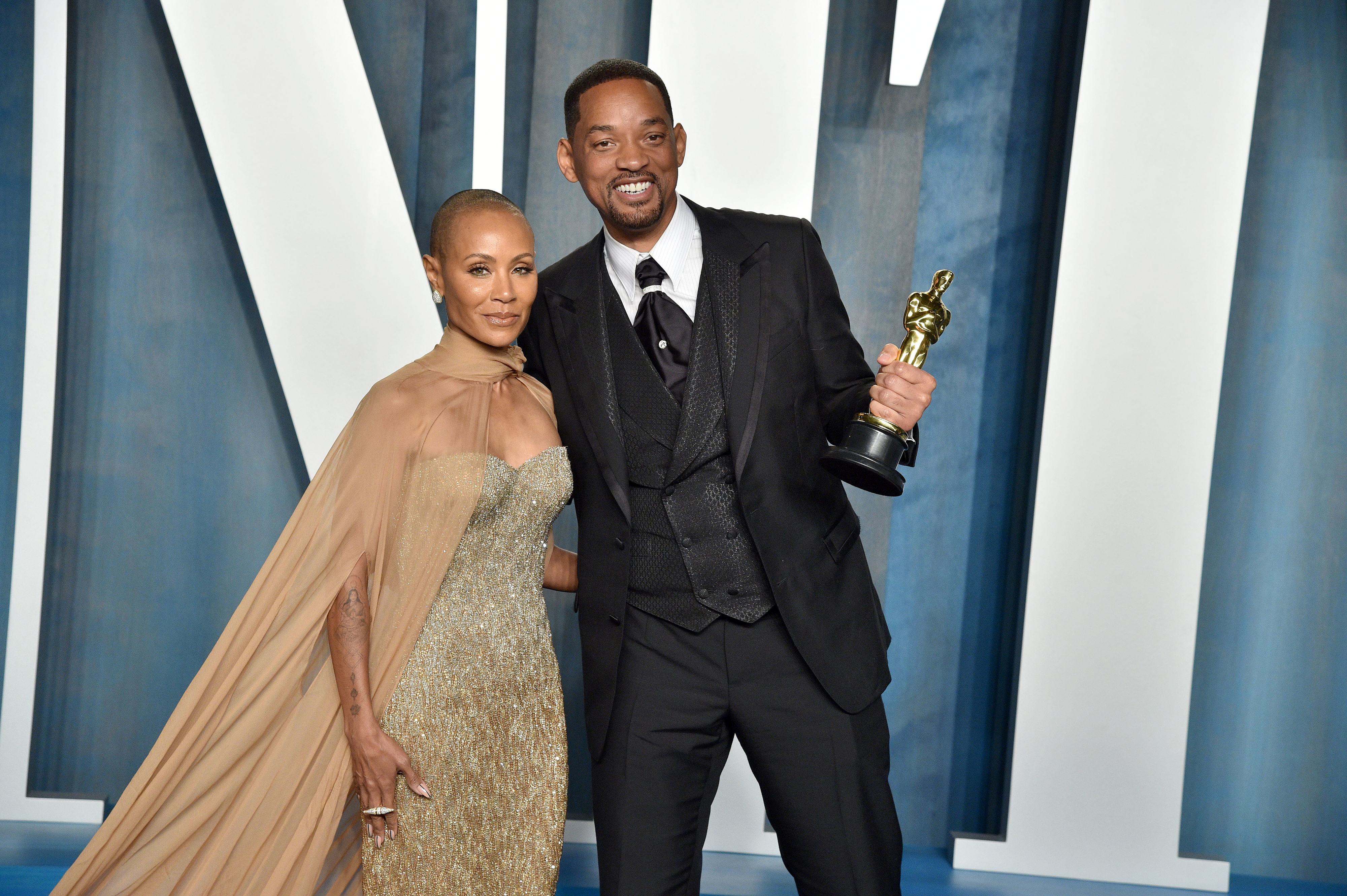 Will smiling and holding his Oscar as she stands with Jada on the red carpet