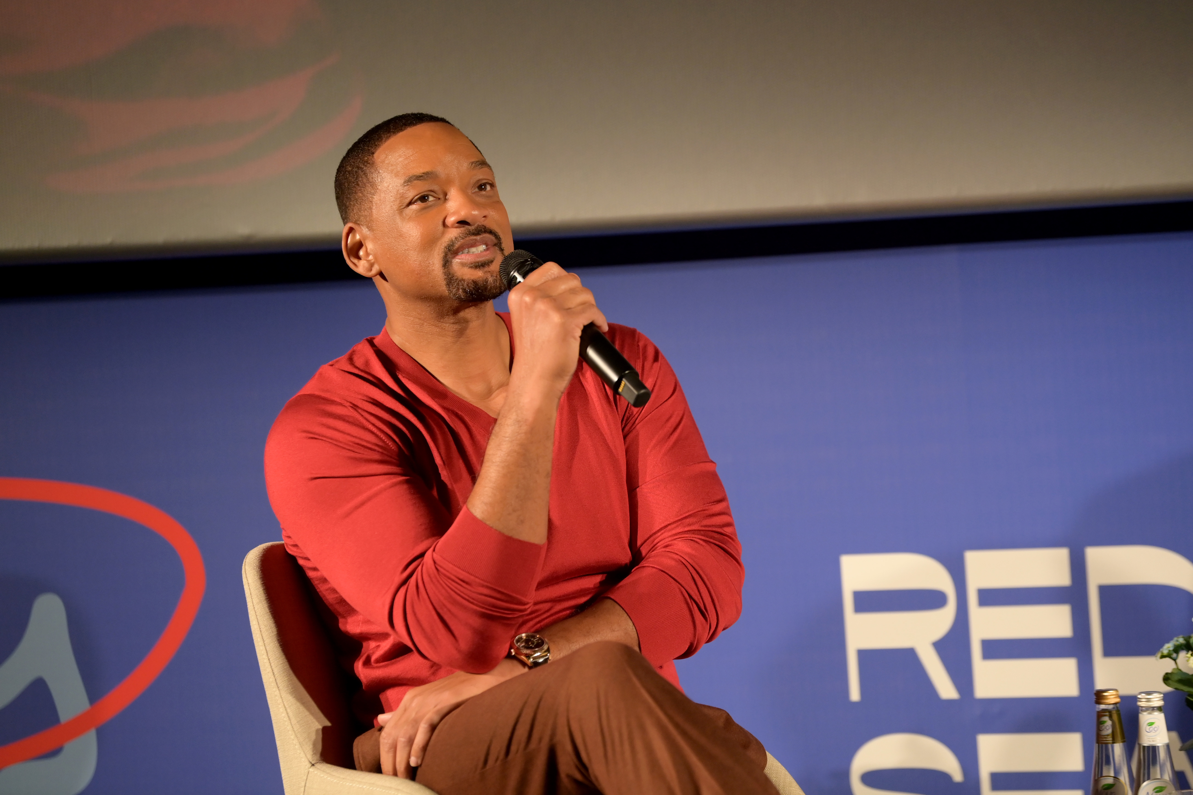 Will seated onstage and speaking into a microphone