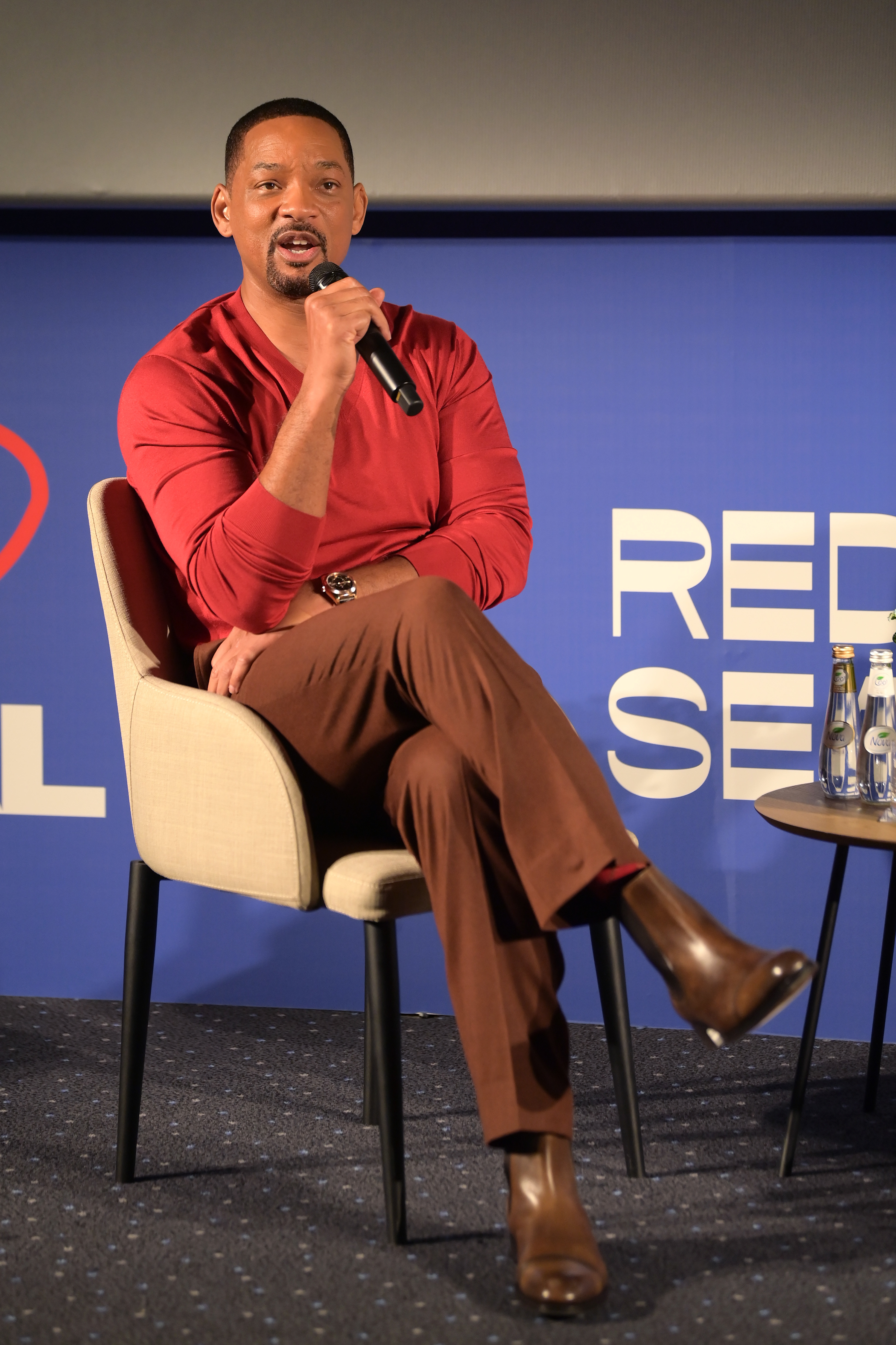 Will seated onstage and speaking into a microphone