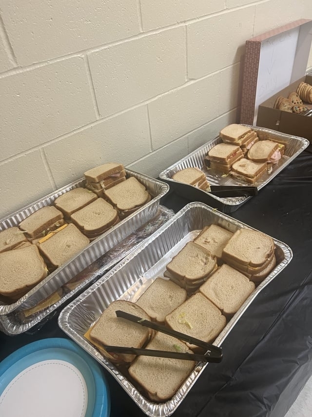 A bunch of cold cut sandwiches in three pans on a table