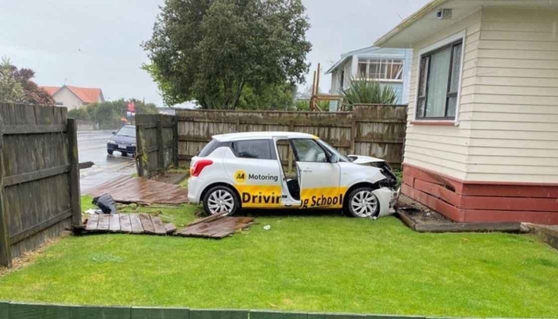 A &quot;driving school&quot; car sitting in the front yard of a house with a demolished fence behind it