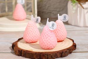 four pastel pink strawberry candles resting on a table 