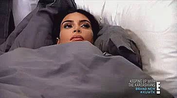 Kim Kardashian lying under the covers in bed, looking off into the universe seemingly contemplating life