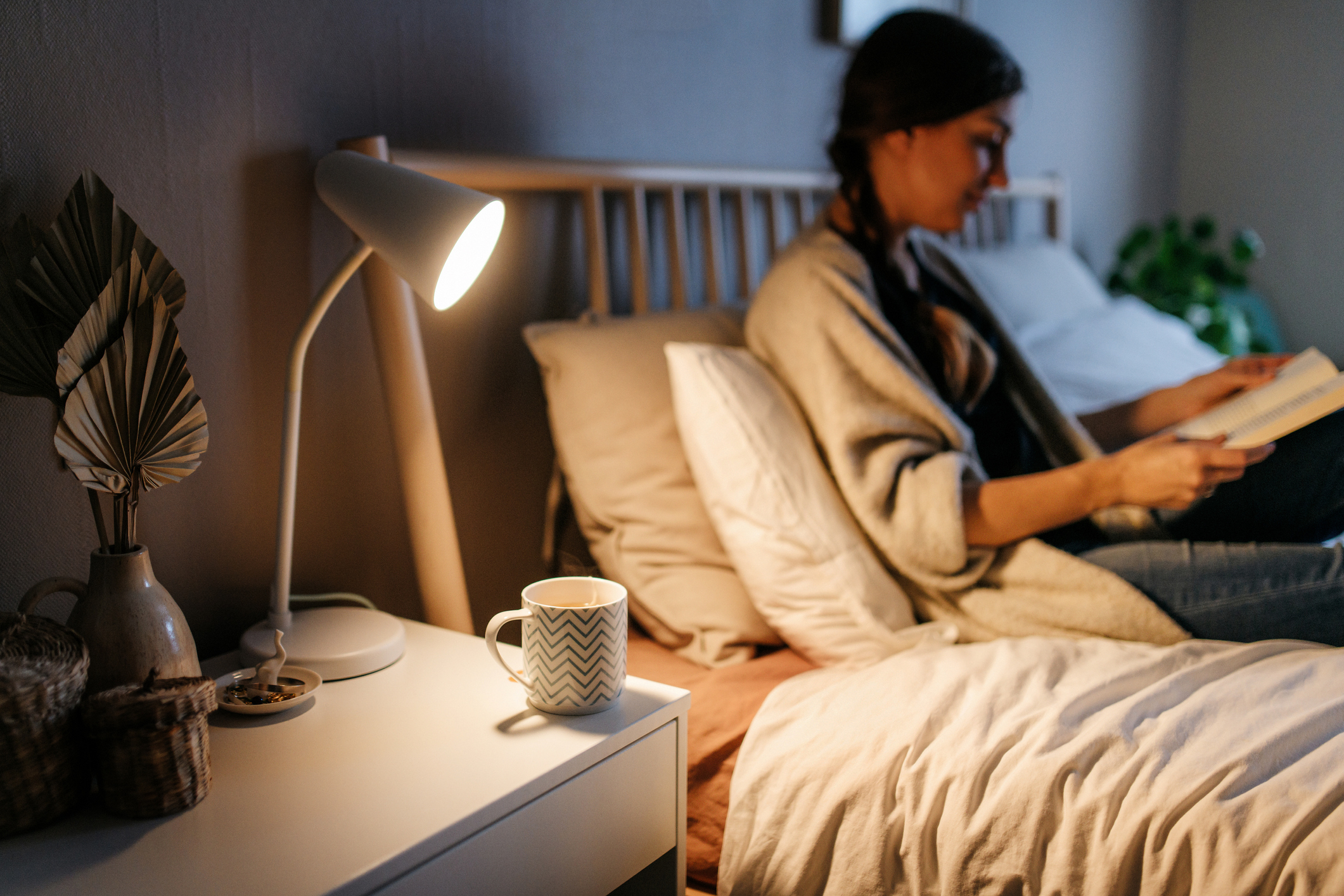 A woman sitting up in bed, reading a book by side table light