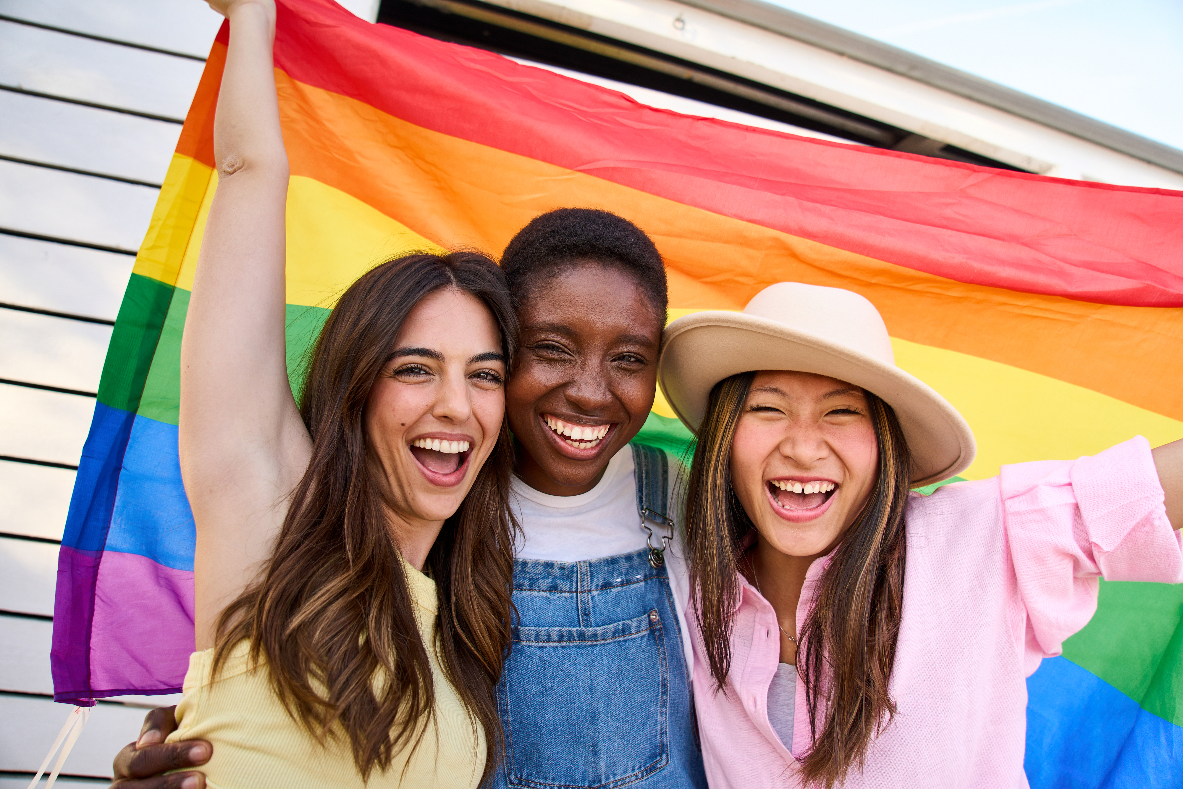 three young women holding up a pride flag