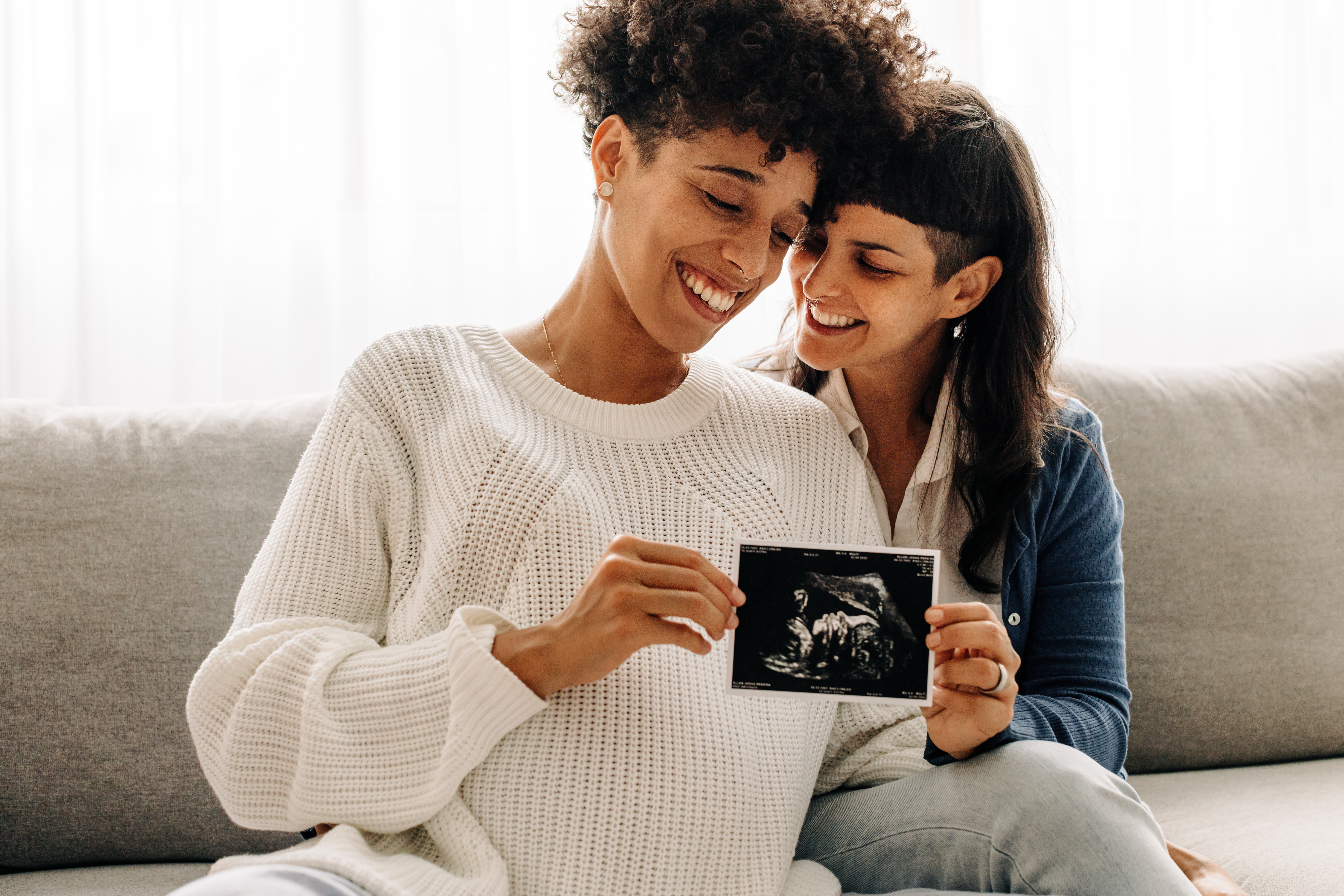 pregnant lesbian couple holding up a picture of a fetal ultrasound