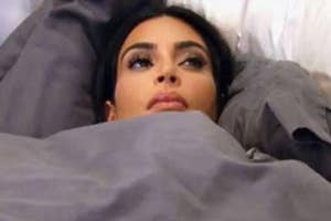 Kim Kardashian laying in bed under the covers staring off into the distance contemplating life