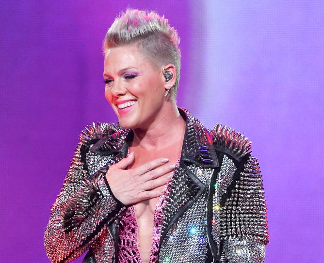 pink with her hand over her heart on stage as she smiles