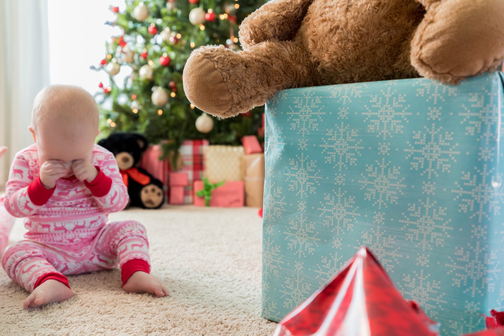 baby rubbing their eyes while sitting up in front of a large present