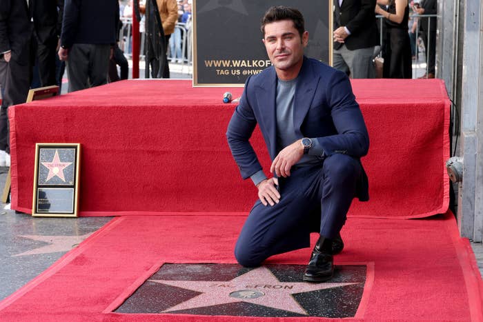 Close-up of Zac kneeling on red carpet next to his star on the Walk of Fame