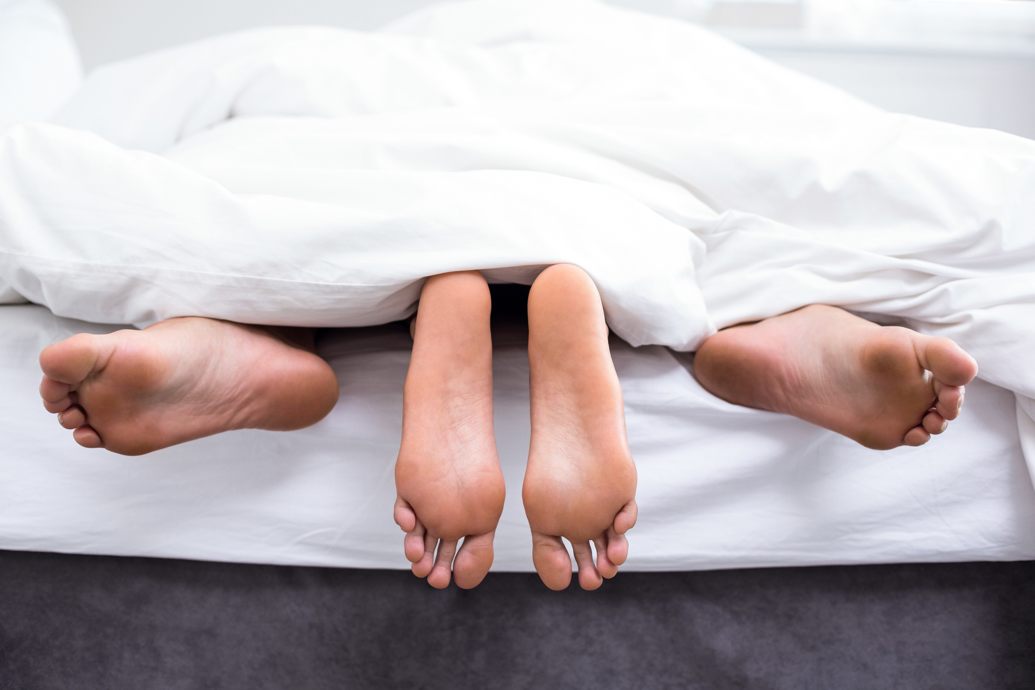 Two pairs of feet peeking out from the covers on a bed
