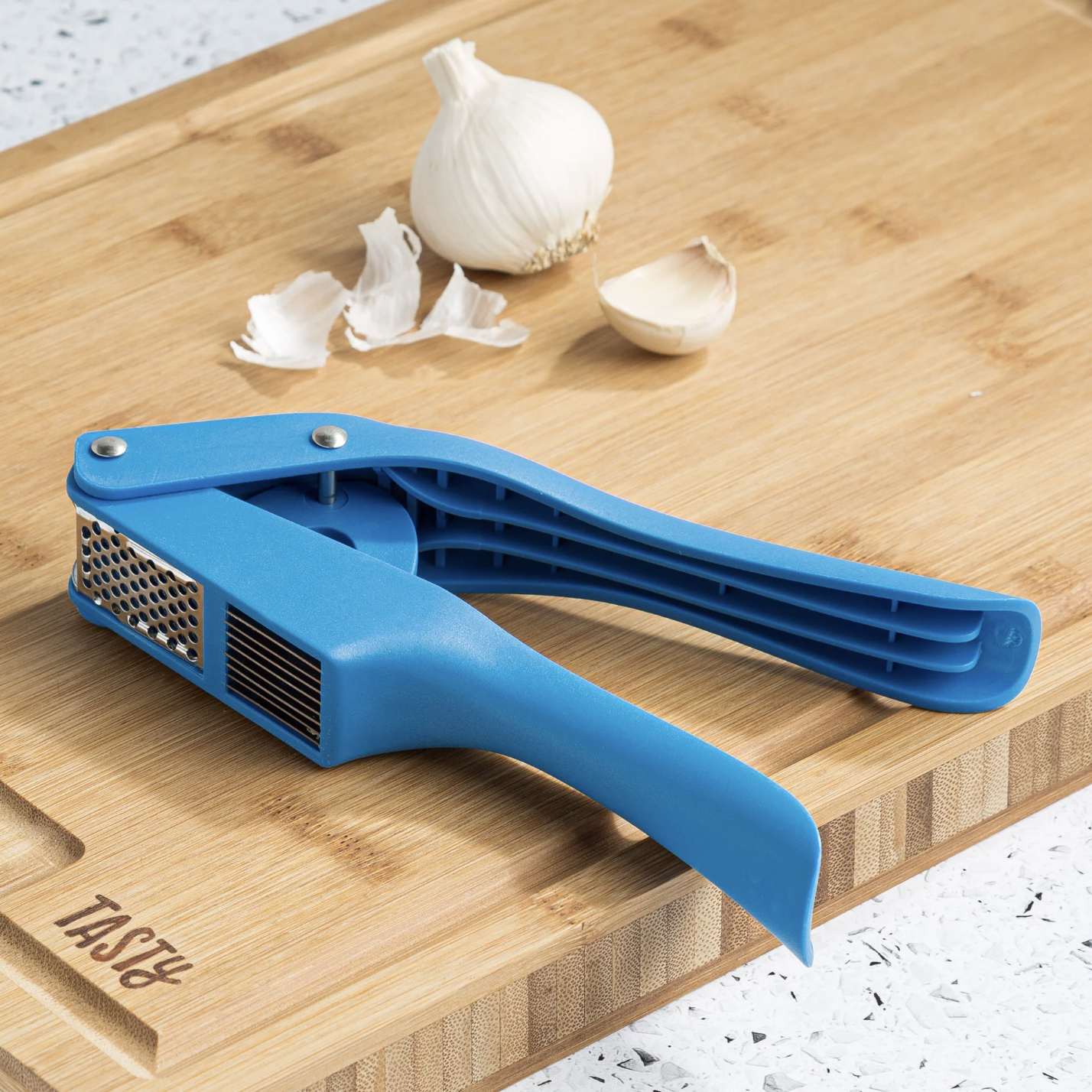 The blue garlic press on cutting board next to garlic cloves